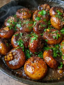 Macro shot of whole button mushrooms in a cast iron skillet with seared edges and garlic bits. (Texas Roadhouse mushroom recipe)
