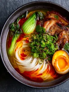 Macro close-up of Chinese Rice Noodle Soup showing glistening broth droplets and silky thin noodles.
