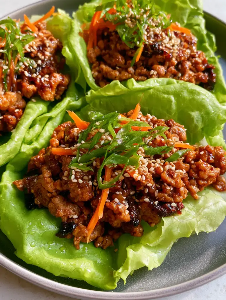 Top-down view of vibrant lime-green lettuce cups garnished with orange julienned carrots and green scallions. (ground turkey lettuce wraps)
