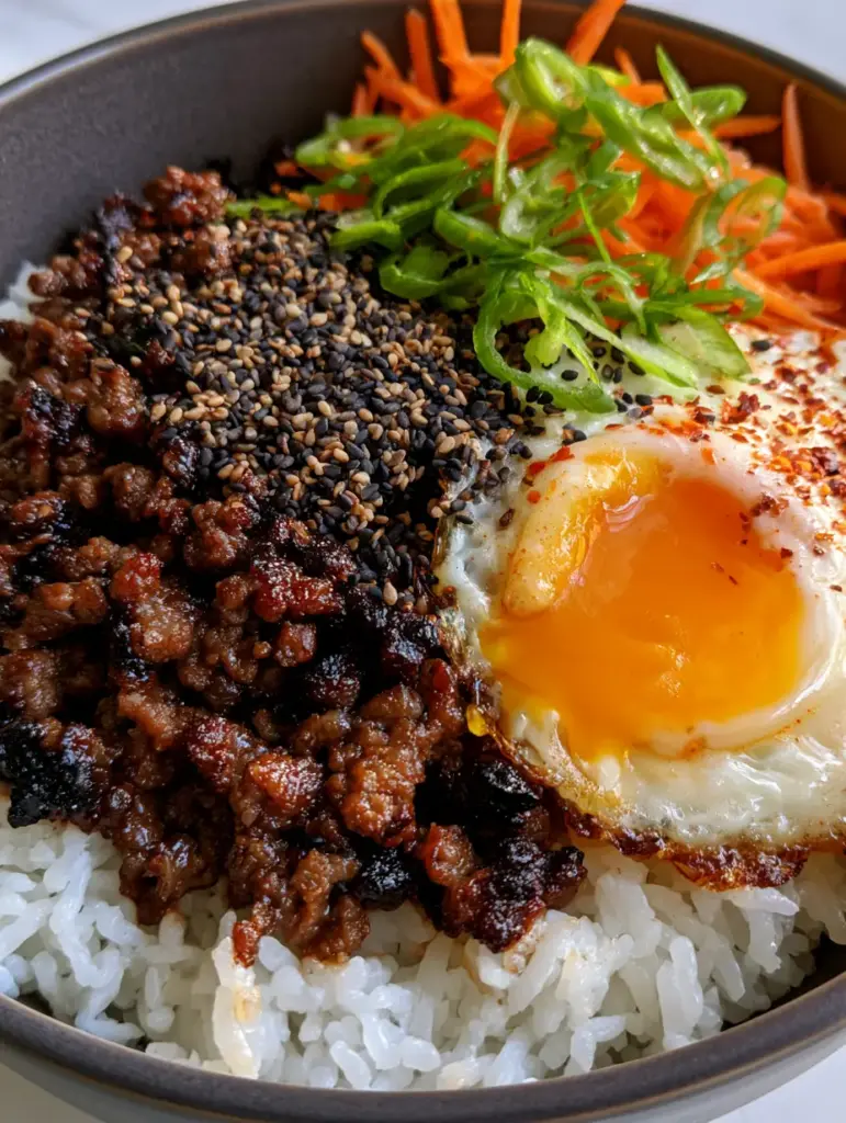 Close up of a runny orange egg yolk over white jasmine rice and julienned carrots.