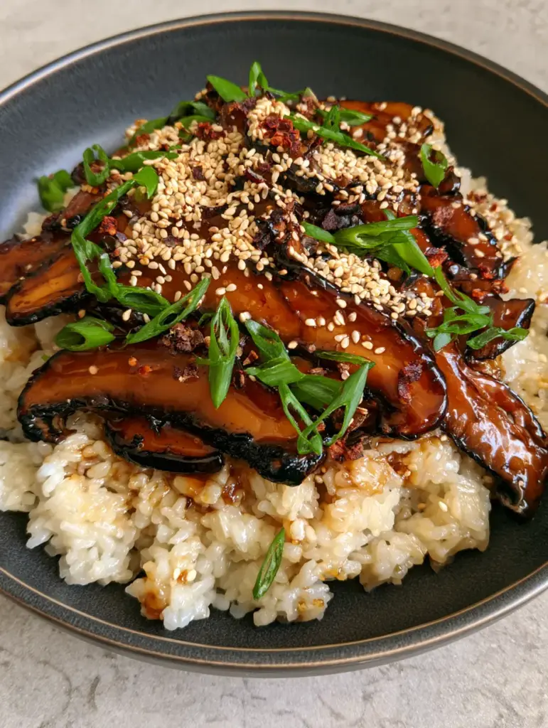 Individual grains of glistening short-grain rice topped with glossy glazed mushrooms and green scallions.